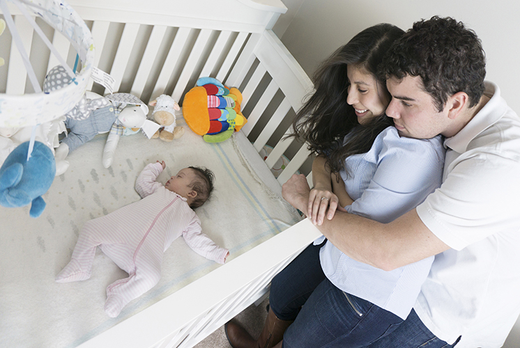 parents look at new baby sleeping in crib