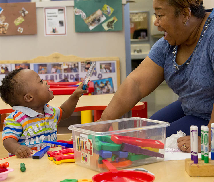 a teacher mirrors happy surprise as toddler plays with magnets