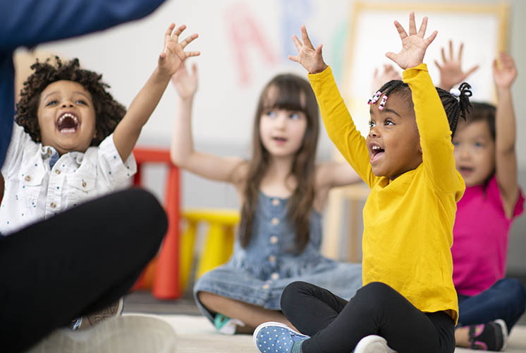 laughing kids sitting on the floor raise their arms