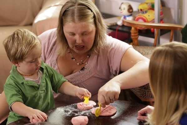 Maestra enseñándole a un niño cómo cortar plastilina