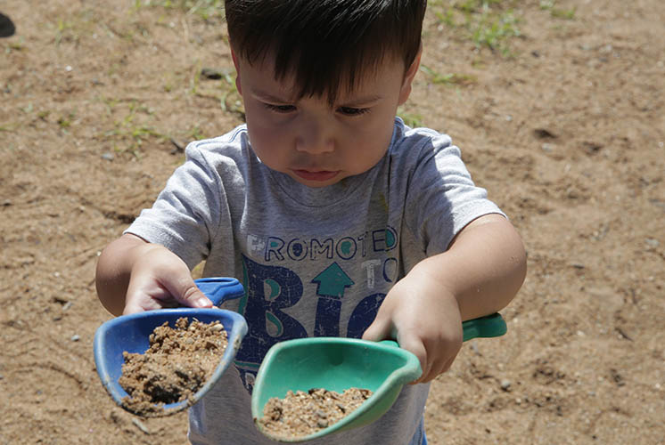 a boy lifts two plastic scoops of dirt and sand