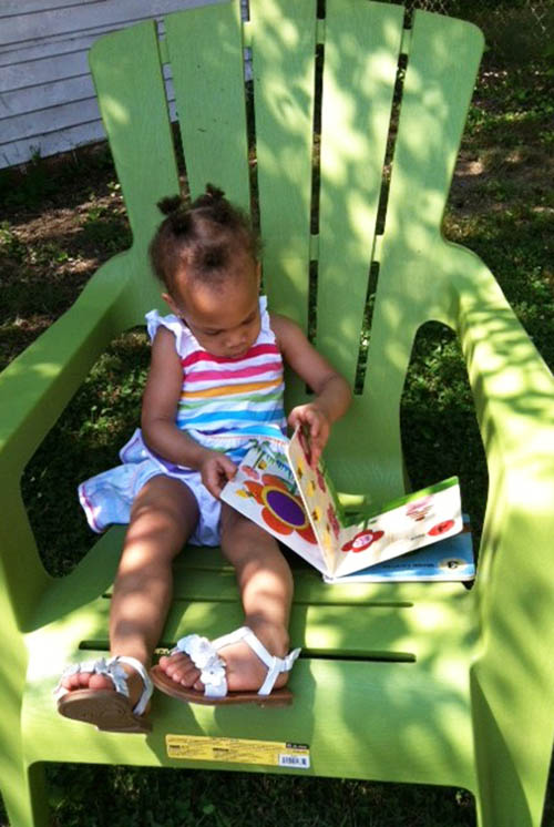 a girl sits on a chair in the shade to look at a book