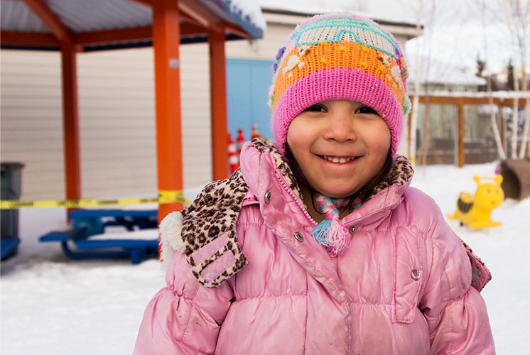 Una niña sonriente se encuentra en un patio de juego cubierto de nieve