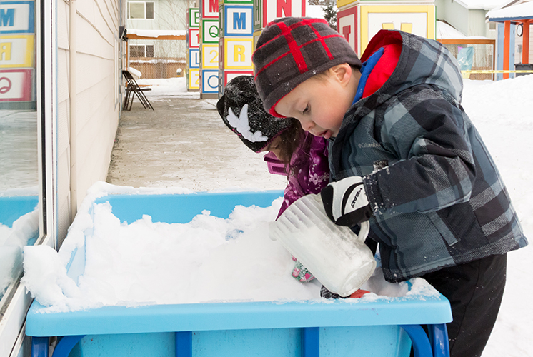 Dos niños juegan con la nieve y una jarra