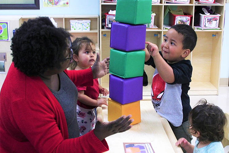 a boy stacks blocks while a teacher helps them stay upright