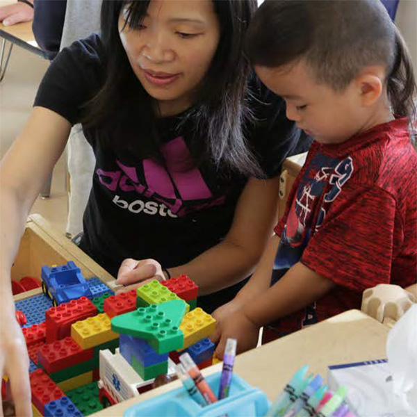 Teacher showing a toddler boy how to stack blocks 