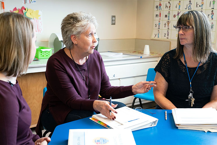 three women having a discussion while sitting around a table with notebooks