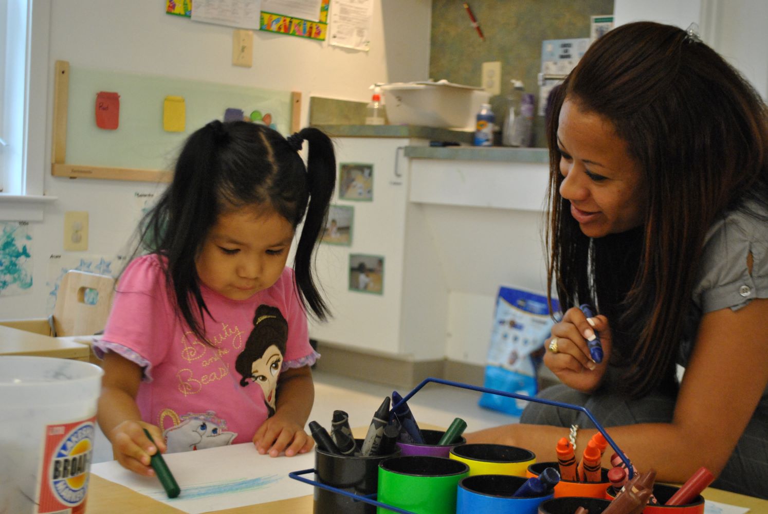 Maestra ayudando a una niña a colorear con crayones.