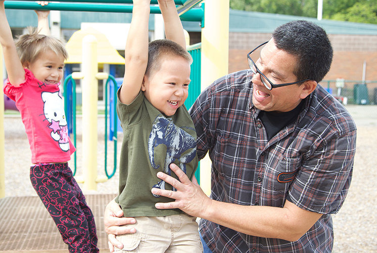 a teacher helps two kids play on bars on playground