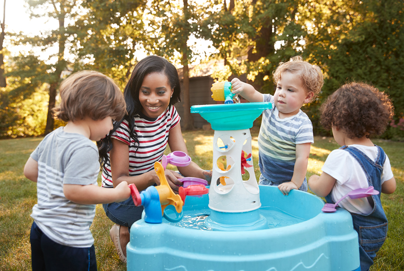 Teacher and 3 children playing outdoors at a mini fountain.