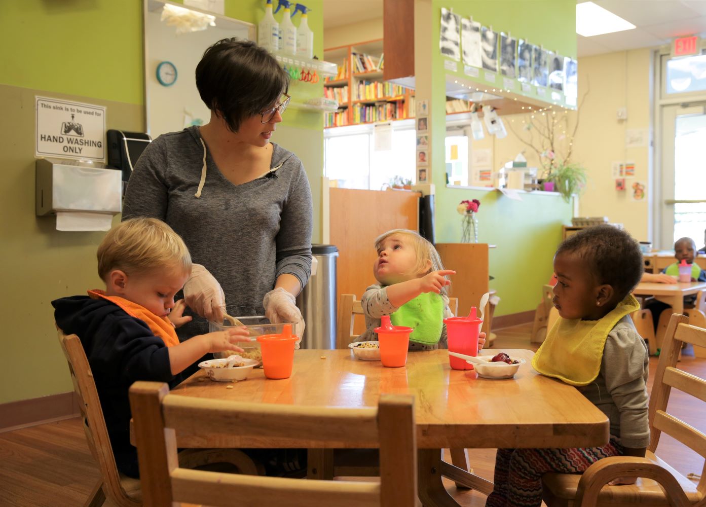 Teacher preparing food for children seated at table.