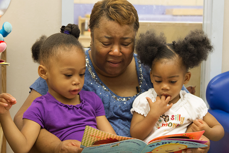 A teacher reads to two girls on her lap