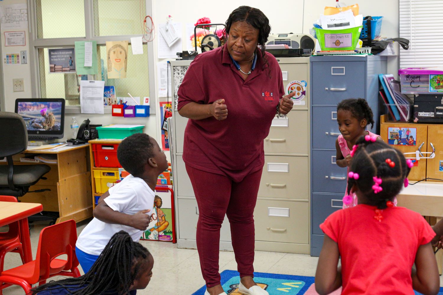 Teacher showing children how to cluck like a chicken using their arms as wings.