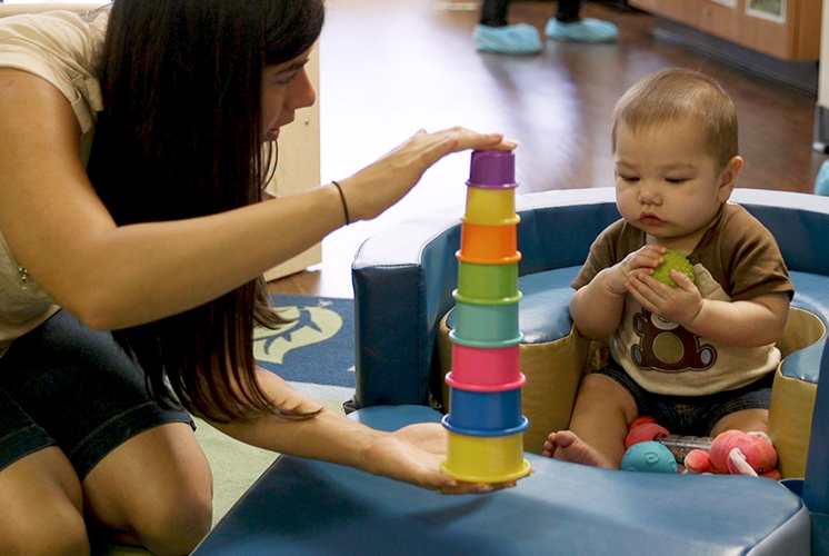 A teacher shows stacking cups to a toddler