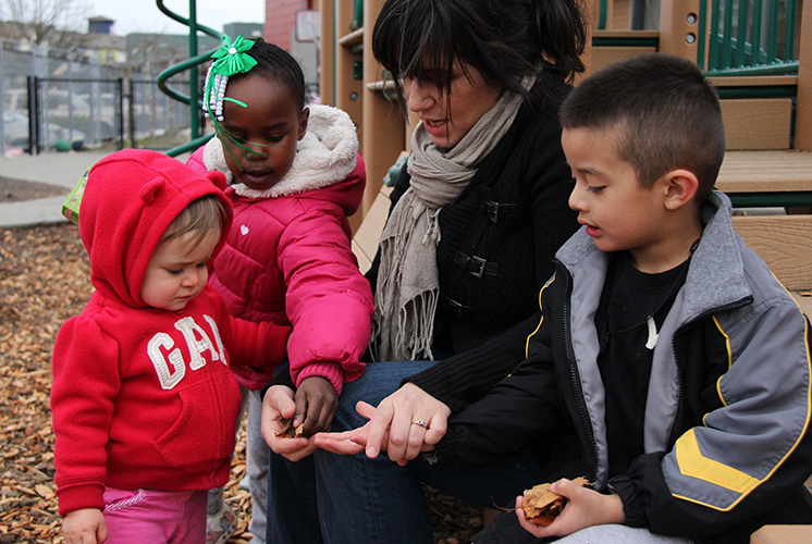 A teacher and three students examine leaves together outside