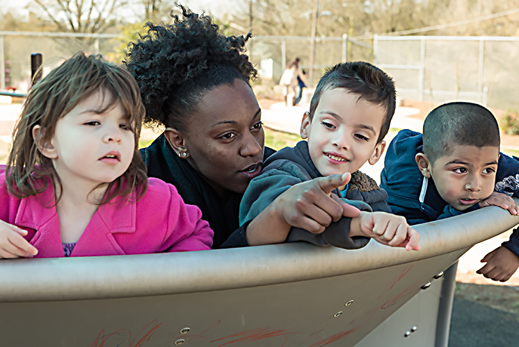 three kids and a teacher playing on the playground