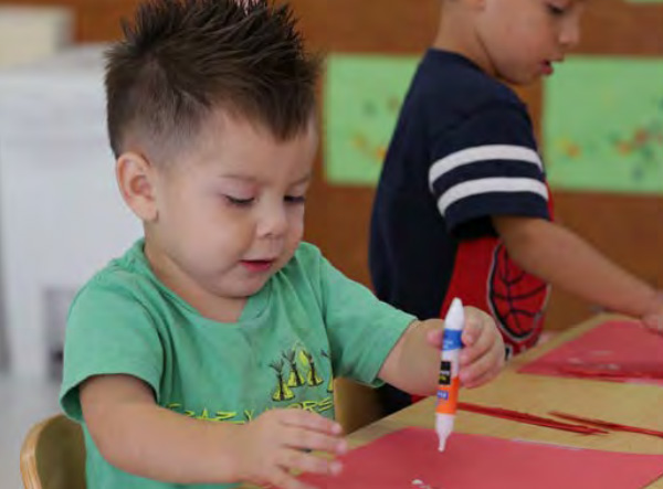 Niño pequeño haciendo un proyecto de arte con pegamento y papel para manualidades rojo