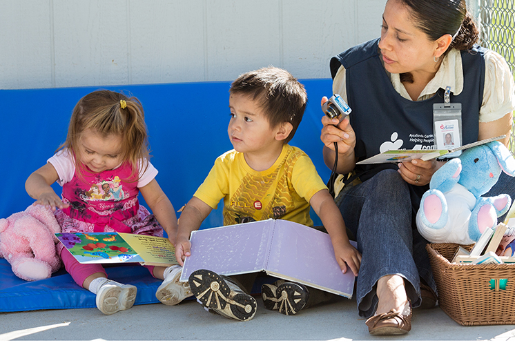 two children with books sitting next to teacher