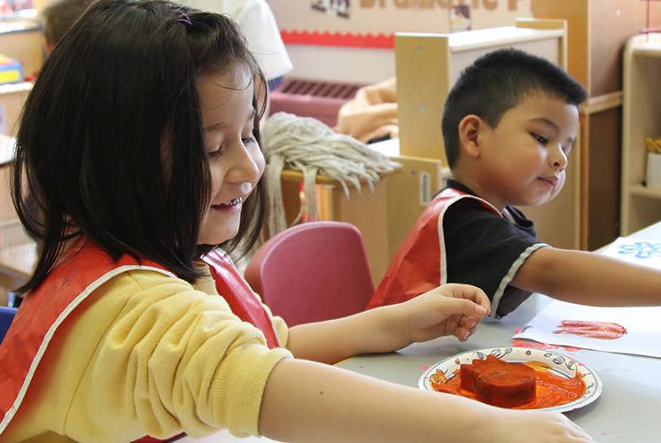 A boy and girl play with paint and sponges at a table