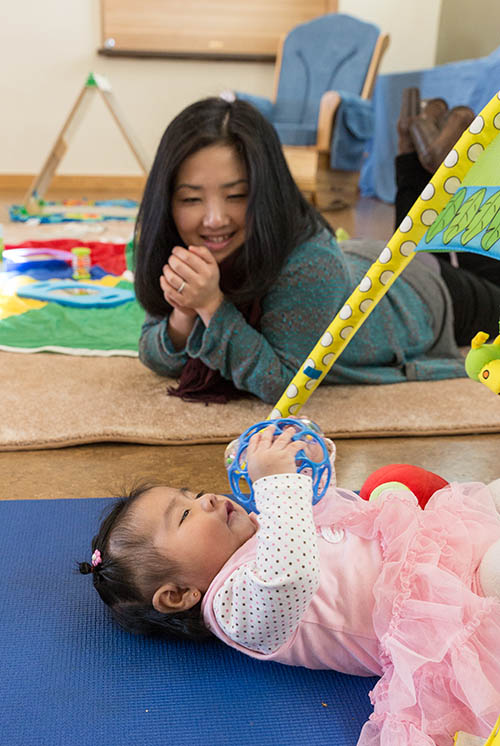 a woman laying on the floor watches a baby on her back playing