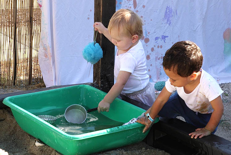 children play with water in a tub lying on top of a sandbox