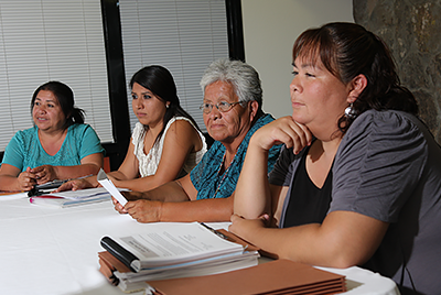 Four women sitting at an office table listening to someone off camera