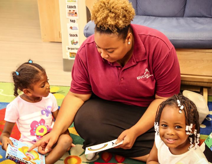 Woman helps child read while hte other kid stares at the camera