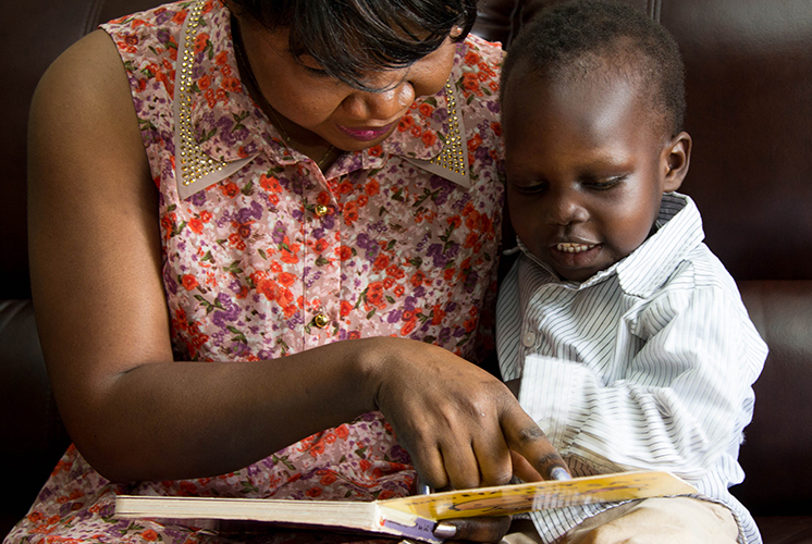 A woman reads with a boy seated on her lap