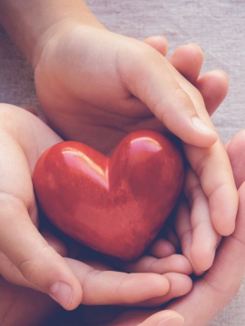 Two hands holding a red ceramic heart.